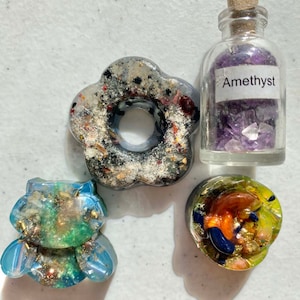 May include: Four resin crafts, including a flower-shaped ring holder, a small bear, a round charm, and a small glass bottle filled with amethyst crystals. The bottle has a cork stopper and a label that reads "Amethyst".