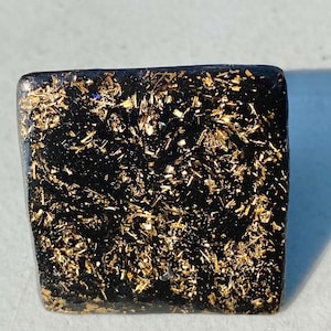 May include: A square black ring with gold glitter embedded in the resin.