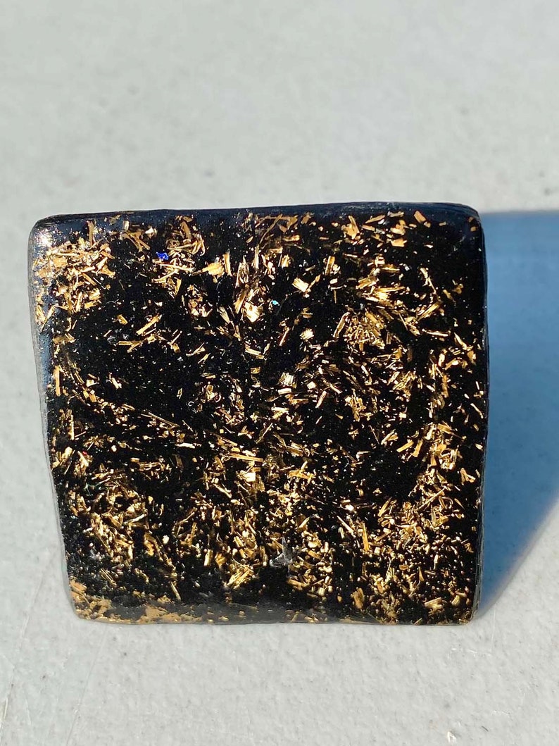 May include: A square black ring with gold glitter embedded in the resin.