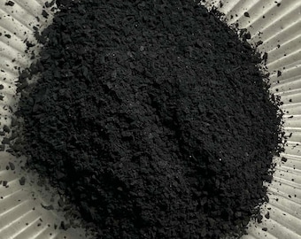May include: A close-up view of a pile of black charcoal powder in a white bowl. The charcoal is finely ground and has a smooth, even texture.