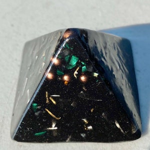 May include: Black pyramid with green and gold glitter embedded inside. The pyramid is made of resin and has a smooth, polished surface.