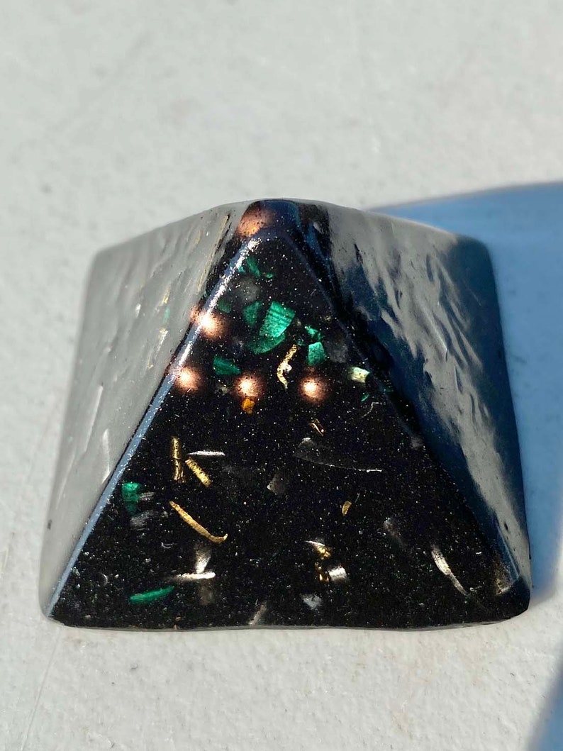 May include: Black pyramid with green and gold glitter embedded inside. The pyramid is made of resin and has a smooth, polished surface.
