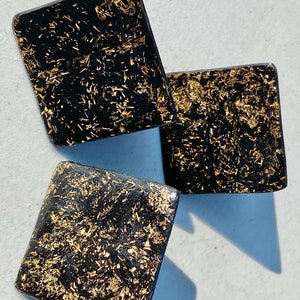 May include: Three black square-shaped earrings with gold glitter embedded in the surface.