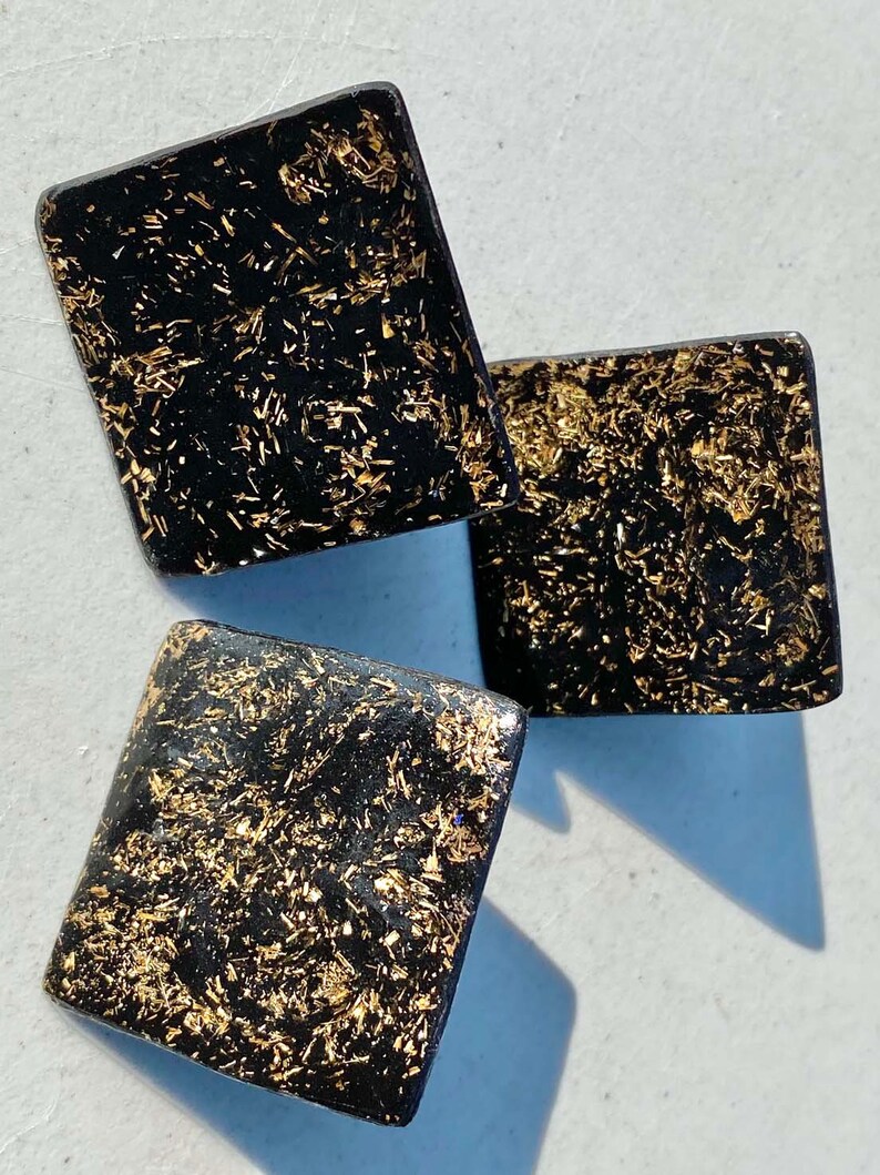 May include: Three black square-shaped earrings with gold glitter embedded in the surface.