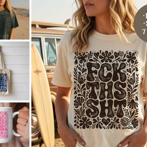 May include: A cream-colored short-sleeve t-shirt featuring a dark brown graphic print with the text FCK THS SHT surrounded by floral and heart motifs. The design is also shown on a dark green t-shirt, a white tote bag, and a white ceramic mug.