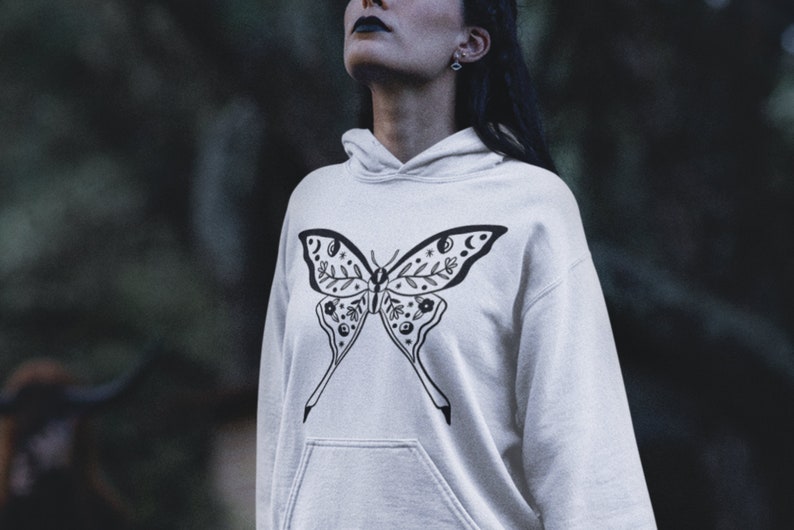 Może przedstawiać: Biała bluza z kapturem z czarno-białym wzorem motyla. Motyl ma skomplikowane detale, w tym elementy kwiatowe i symbole niebieskie.