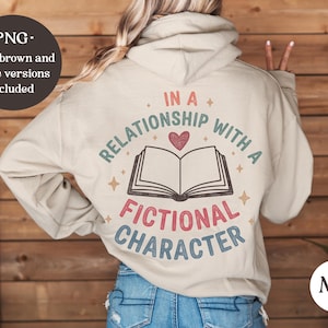 以下が含まれることがあります： レトロなフォントで「IN A RELATIONSHIP WITH A FICTIONAL CHARACTER」と書かれたベージュ色のパーカー。デザインには開いた本、ハート、星が含まれています。パーカーには「PNG」ロゴも付いています。