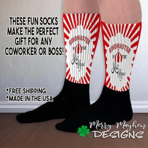 May include: A pair of black socks with red and white stripes. The socks feature the text "Ringmaster of the Shit Show" with a circus tent graphic.
