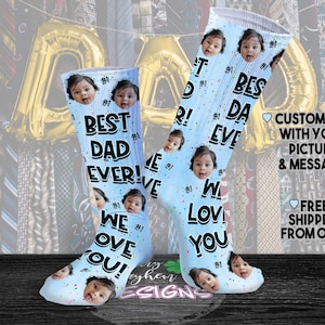 May include: A pair of blue socks with a white confetti pattern and a black and white graphic print. The socks feature the text "Best Dad Ever!" and "We Love You!" with a photo of a child on each sock.