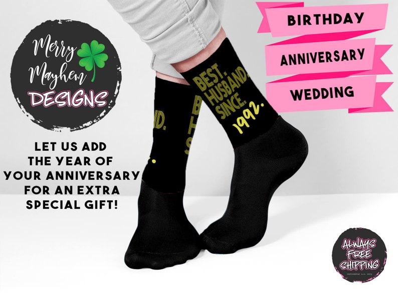 May include: A pair of black crew socks featuring the yellow text "BEST. HUSBAND. SINCE. 1992." printed on the side. The socks are worn on the feet, which are positioned against a white background with pink banners labeled "BIRTHDAY", "ANNIVERSARY", and "WEDDING".