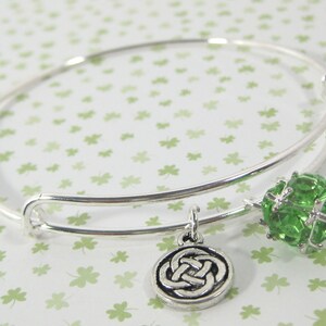 May include: A silver bangle bracelet with a green crystal charm and a silver Celtic knot charm.