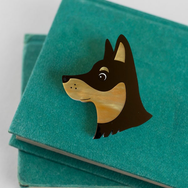 May include: A brown and tan dog head brooch with a black outline, sitting on top of two teal blue books.