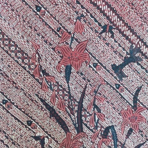 Op de afbeelding: Een close-up van een rood en wit gepatroneerd stof met een bloemenontwerp. De stof heeft een herhalend patroon van gestileerde bloemen en bladeren, met een zwarte omtrek. De achtergrond is een wit en rood gestreept patroon.