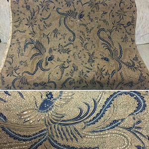 Op de afbeelding: Een bruine stof met een blauw en gouden patroon van gestileerde vogels en bloemen. De stof heeft een subtiele glans.