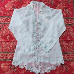 Könnte beinhalten: Eine weiße, durchsichtige Bluse mit zarten Spitzendetails an Ausschnitt, Ärmeln und Saum. Die Bluse ist aus leichtem Stoff gefertigt und hat eine lockere Passform.