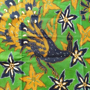 May include: A green fabric with a black and gold peacock design. The peacock is depicted with its tail feathers spread out. The fabric has a batik style.