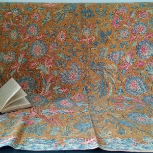 May include: A brown fabric with a blue and pink floral pattern. The fabric has a subtle sheen and a soft texture. A book is lying on the fabric.