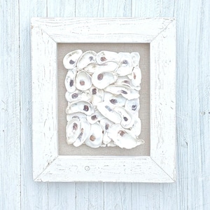 May include: A white framed picture with a beige background featuring a collection of white oyster shells.