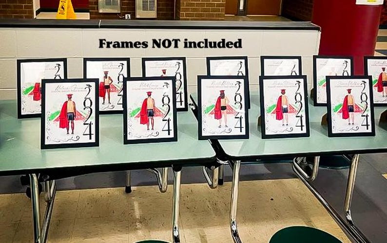 May include: Multiple framed graduation art prints featuring a figure in a graduation gown and the year 2024. The art has a red and black color scheme. The frames are black and are displayed on a light green table.