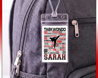 May include: A clear plastic luggage tag with a white insert featuring the word TAEKWONDO at the top, a black silhouette of a person performing a kick, and various red and black words related to martial arts, with the name SARAH printed at the bottom.