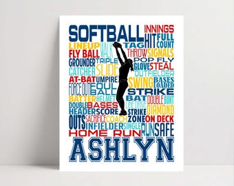 May include: A white rectangular print featuring a black silhouette of a softball player catching a ball. The design includes blue, red, and yellow text with softball-related terms like SOFTBALL, INNINGS, HIT, and the name ASHLYN at the bottom.