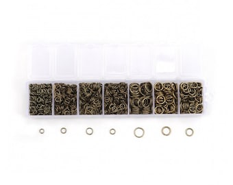 May include: A clear plastic organizer filled with small, bronze-colored jump rings. The organizer has seven compartments filled with varying quantities of the rings. Several individual jump rings are also displayed below the organizer.