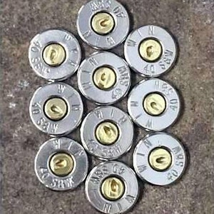 May include: A collection of nine silver-colored bullet casings with gold-colored primers. Each casing is marked with the text "WIN 40 S&W". The casings are arranged in a circular pattern on a textured, gray surface.
