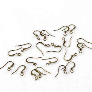 May include: A collection of antique bronze-colored earring hooks, scattered on a white surface. The hooks vary in shape, with curved wires and small decorative beads. These components are for jewelry making.