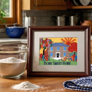 May include: A framed cross-stitch artwork depicts a colorful house with a blue roof, surrounded by trees and a rising sun. The text "HOME SWEET HOME" is stitched below the house. The frame is dark brown.
