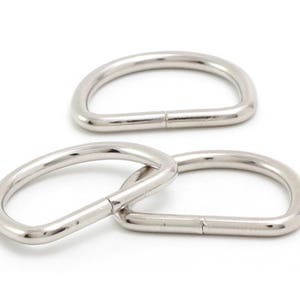 May include: Three silver-colored D-rings are displayed against a white background. The D-rings are made of metal and have a smooth, shiny surface. Two rings are interlocked, and the third is positioned above them.