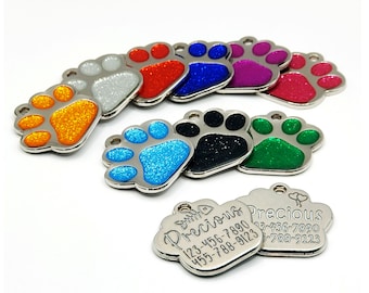 Peut inclure: Assortiment de médailles pour chien en forme de patte avec une finition pailletée. Les médailles sont argentées avec des incrustations de paillettes de différentes couleurs. Les médailles ont un trou pour être attachées à un collier. Deux médailles ont un texte gravé qui dit "Precious" avec des numéros de téléphone.