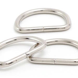 May include: Three silver metal D-rings, also known as D rings or D-shaped rings, are shown on a white background. These rings are commonly used in crafting, sewing, and jewelry making.