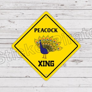Op de afbeelding: Geel ruitvormig bord met zwarte rand en tekst "PEACOCK XING". Het bord toont een blauwe pauw met een kleurrijke staart. De achtergrond is een wit houten oppervlak.