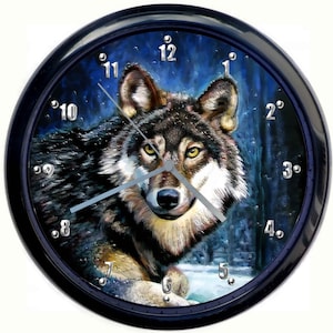 Op de afbeelding: Een zwarte geframed klok met een wolfillustratie op de wijzerplaat. De wolf kijkt rechtstreeks naar de kijker met een blauwe en zwarte achtergrond. De wijzerplaat van de klok heeft zilveren cijfers en wijzers.