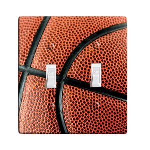 May include: A close-up of a basketball with an orange and black design. The basketball is textured with a pattern of small circles. The image is used for a light switch cover.