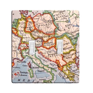 May include: A vintage map of Europe with a light blue background and orange, red, and yellow borders. The map shows the countries of Europe, including Germany, Poland, Czechoslovakia, Hungary, Yugoslavia, Bulgaria, Greece, Italy, and France. The map is printed on a light switch plate with two toggle switches.
