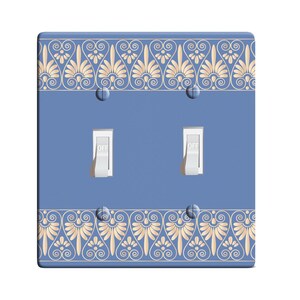 May include: A light blue double light switch cover with a decorative border of a gold Greek key pattern.