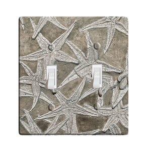 May include: A light switch cover with a design of fossilized starfish on a light brown background. The switch cover has two toggle switches labeled "OFF".