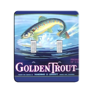 Może przedstawiać: Biało-niebieski włącznik światła z vintage ilustracją pstrąga wyskakującego z wody. Tekst "Golden Trout" jest nadrukowany fioletowymi i różowymi literami. Tekst "Packed and shipped by Harding & Leggett Orange Cove, California" jest nadrukowany czarnymi literami.