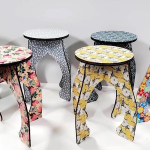 May include: Six colorful, patterned, wooden stools with a unique curved design. Each stool has a different floral pattern.