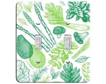 May include: A white light switch cover featuring a green and white pattern of assorted vegetables and herbs. The switch cover has two toggle switches labelled "OFF".