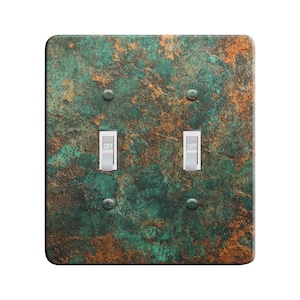 May include: A double light switch cover with a rustic, green and copper-toned design. The cover has a textured, weathered look and features two toggle switches labeled "OFF".