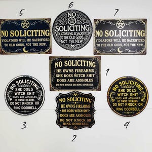 May include: Collection of metal "No Soliciting" signs in various shapes. Signs feature phrases like "Violators will be sacrificed" and "She does witch shit." Designs include pentagrams and crescent moons. The signs are black and gold.