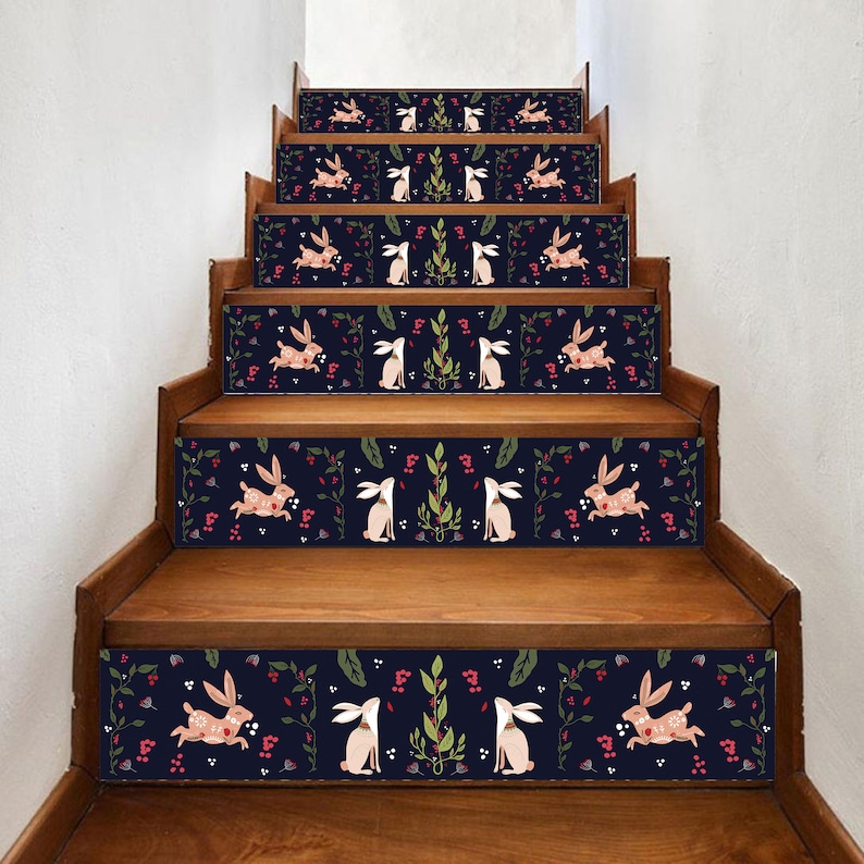 May include: Wooden staircase with decorative stair treads featuring a navy blue background and a repeating pattern of rabbits, leaves, and berries. The rabbits are in pink and white, with green leaves and red berries.