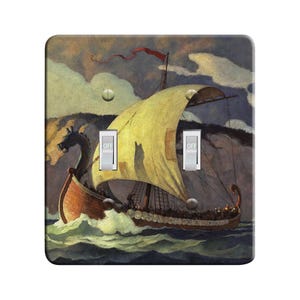 May include: Decorative light switch cover featuring a painting of a Viking ship sailing on a choppy sea. The ship has a yellow sail and a red flag. The switch plate has two switches, both in the off position.