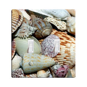 May include: A light switch cover featuring a close-up of a variety of seashells in shades of brown, white, and pink. The switch cover has two toggle switches labeled "OFF".