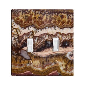 May include: A light switch plate with a brown, white, and gold marble pattern. The plate has two toggle switches, both labeled "OFF".