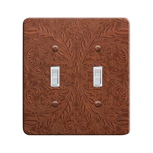 May include: A brown, double light switch cover with an embossed floral pattern. The cover has two silver toggle switches, each labeled "OFF". The design is symmetrical, with the floral pattern mirroring across the center.