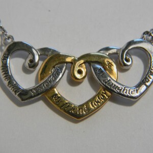 May include: Silver and gold-toned necklace with three interlocking heart pendants. Each heart has an inscription: "Little Girl", "Yesterday", "My Friend Today", "My Daughter", and "Forever". The necklace has a delicate chain.
