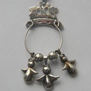 Op de afbeelding: Zilveren hanger ketting met een cirkelvormig ontwerp en drie kleine engel bedels die eronder hangen. De hanger heeft een decoratieve bovenkant met een kroonachtig ontwerp en is opgehangen aan een delicate ketting.